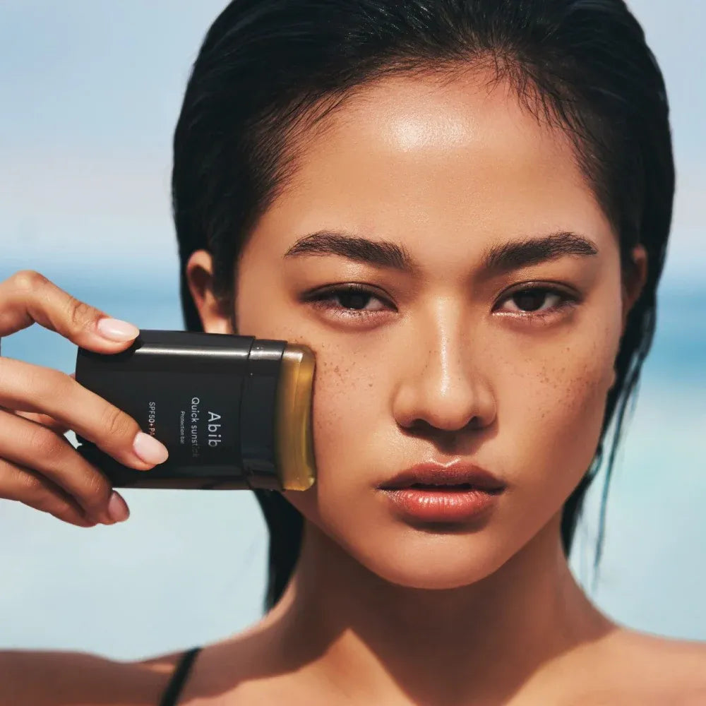 abib Woman holding a black and gold device against her face with a clear blue sky background
